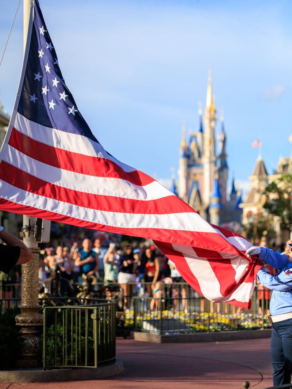 American flag waves in front of Cinderella Castle at Walt Disney World's Magic Kingdom theme park during daytime.
