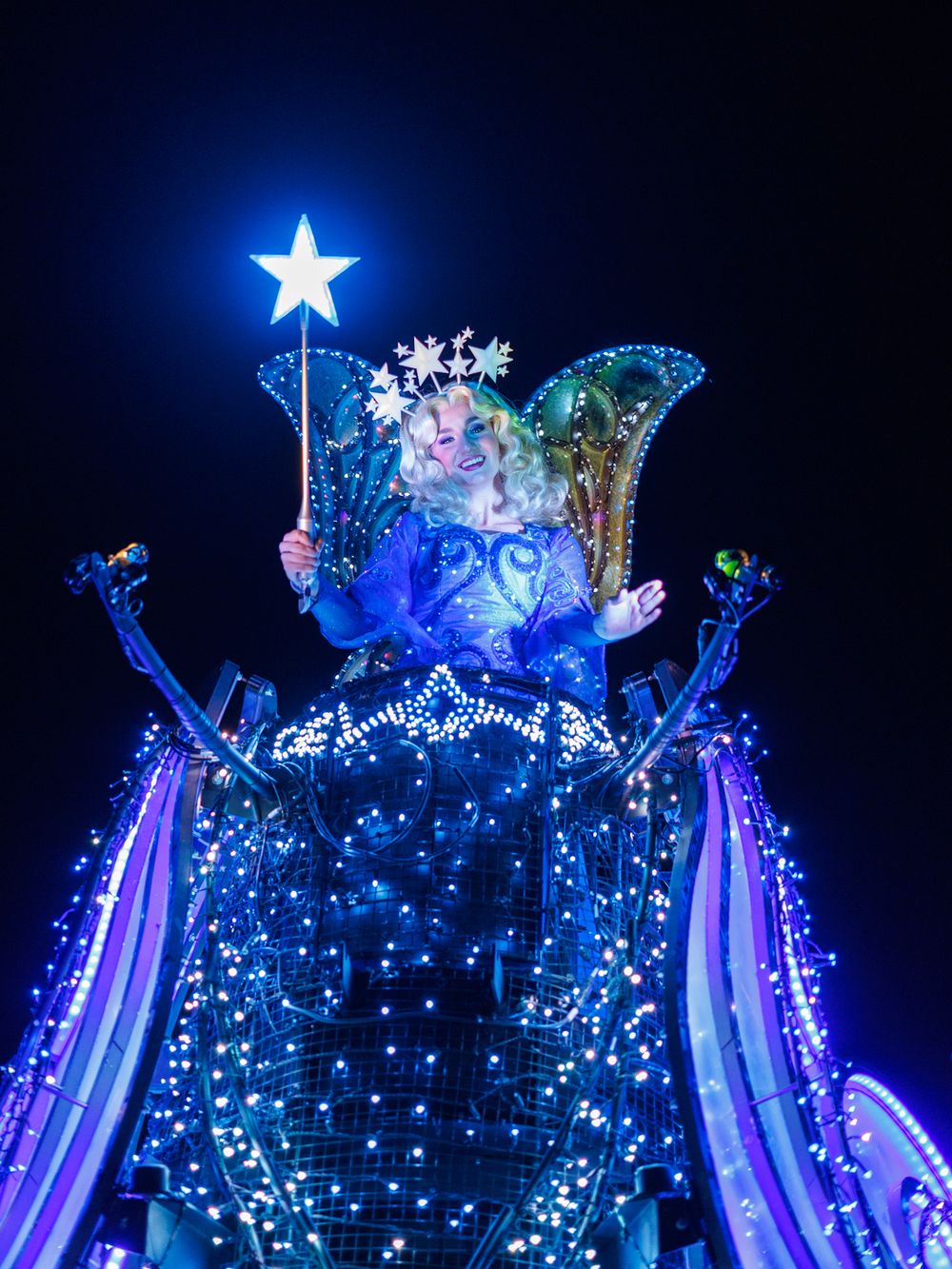 A glowing blue float with a bright star topper features illuminated snowflakes and flowing fabric decorations.