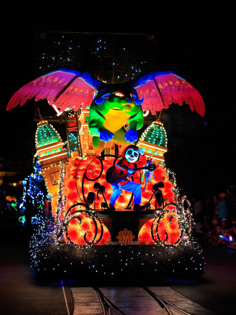 Colorful illuminated parade float featuring palm trees, pumpkins and vibrant decorations at a nighttime festival display.