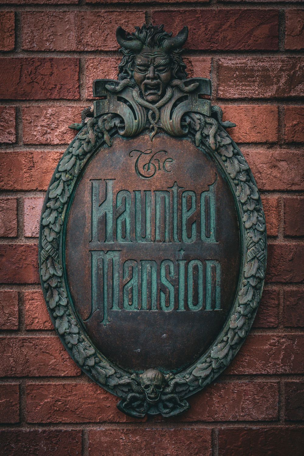 Ornate Haunted Mansion sign mounted on brick wall at Disney theme park.