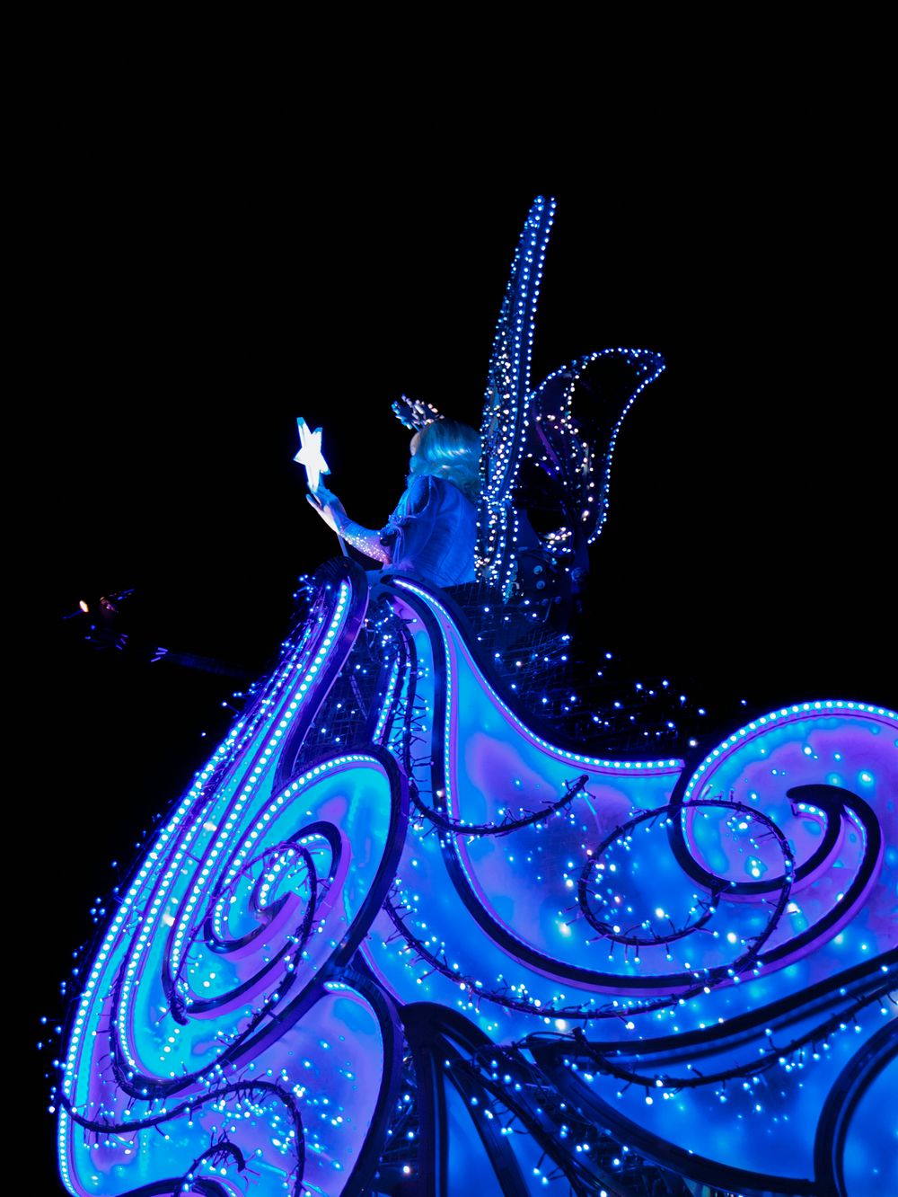 Illuminated blue and purple lights create a swirling pattern against a dark background in a Disney parade display.