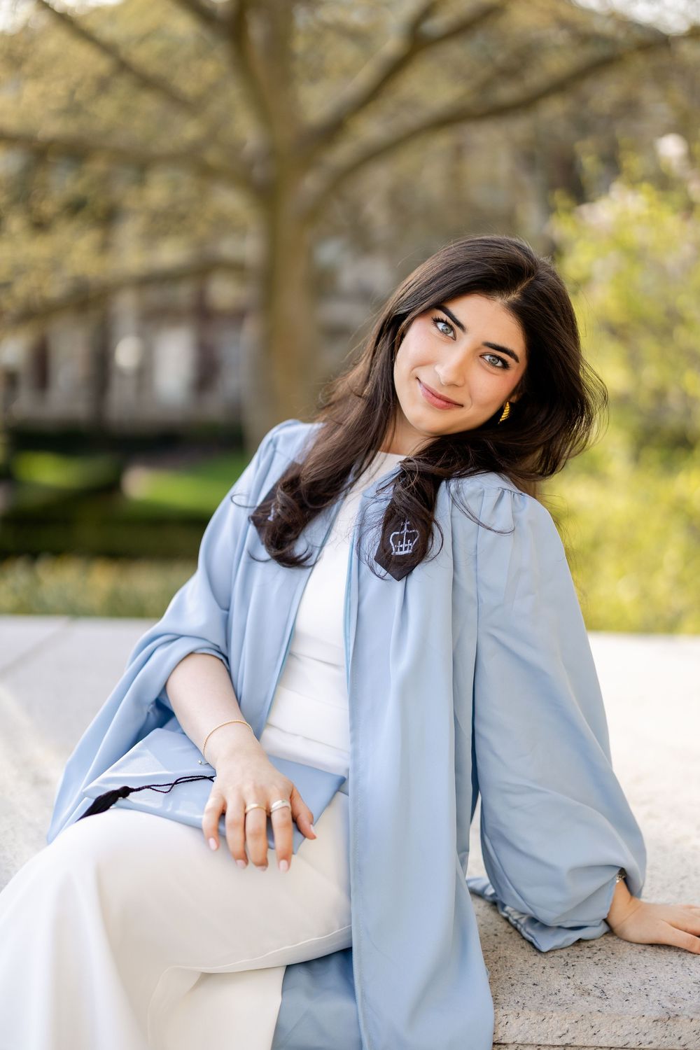 Candid outdoor portrait showing light blue graduation gown against spring campus background.