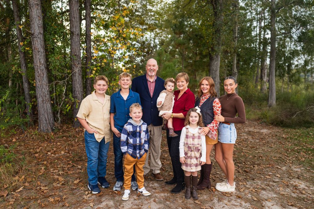 Extended family gathering for outdoor portrait session under trees.