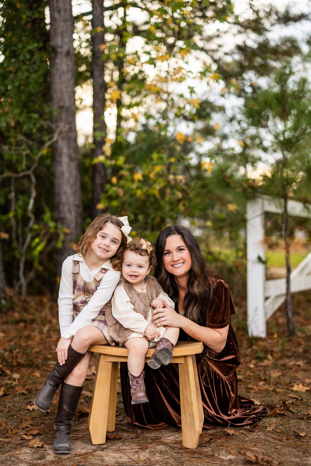 Three people sit on wooden stools for casual portrait in autumn forest.