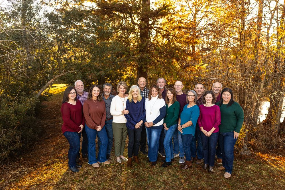 Wide group portrait of extended family members lined up in forest during sunset.