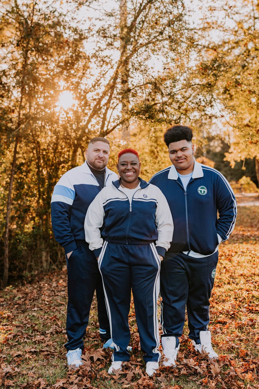 Athletic group in coordinated blue and white tracksuits standing among fall foliage.