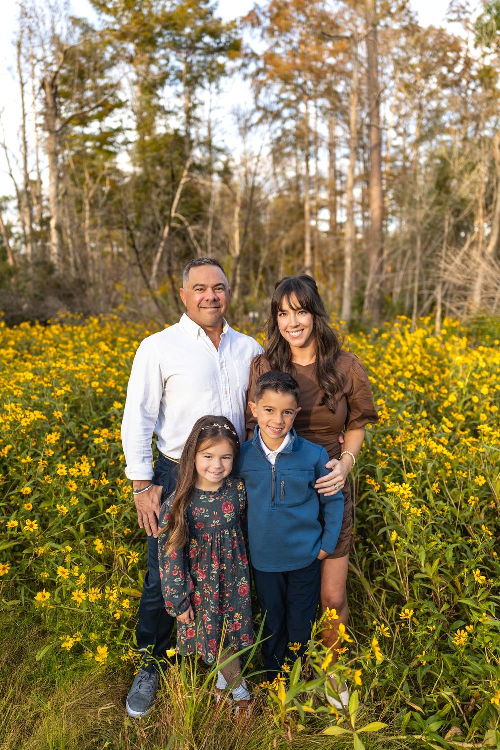 Family photo session in field of yellow wildflowers during golden hour.