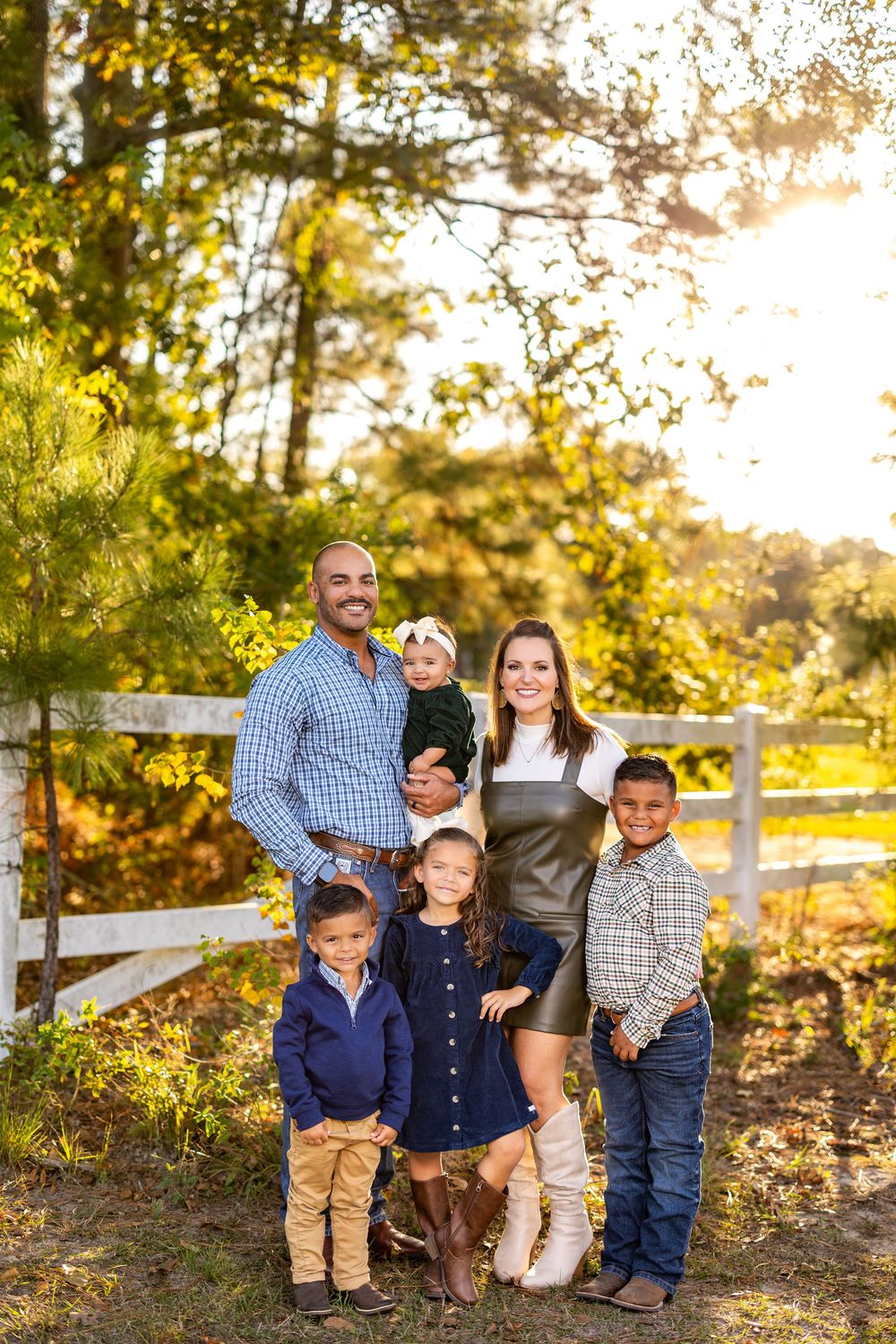 Family portrait session in front of white fence with fall foliage backdrop.