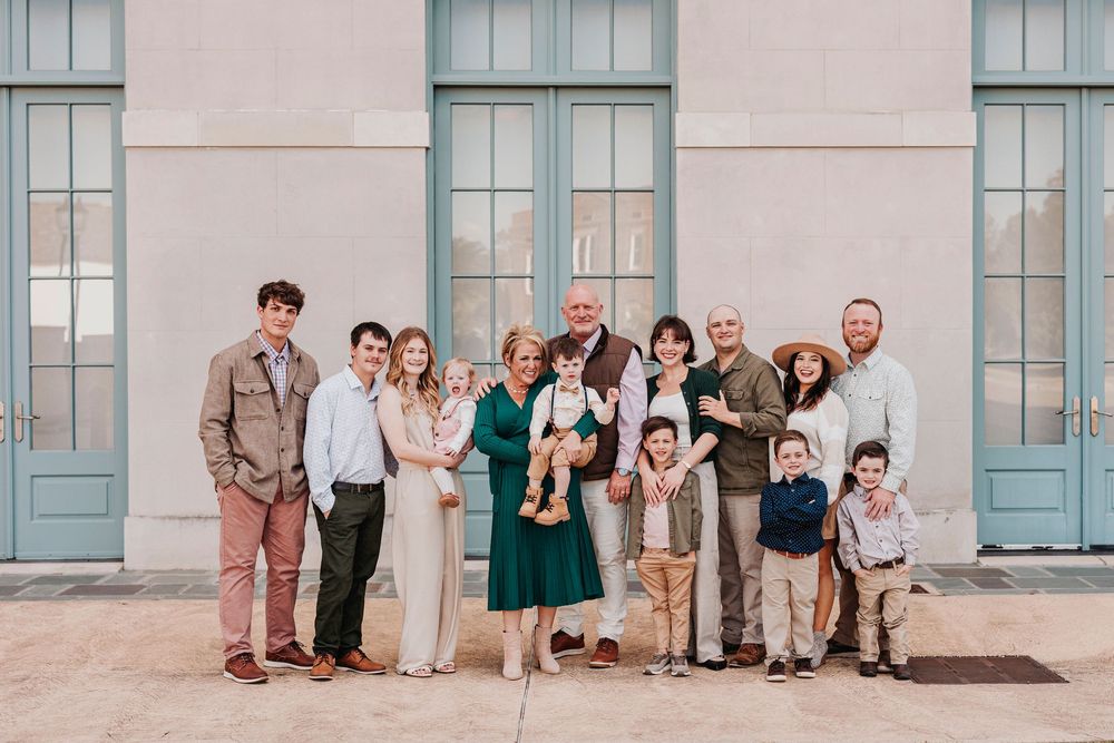 Multiple generations of a family gathered for a casual portrait against a neutral building exterior.