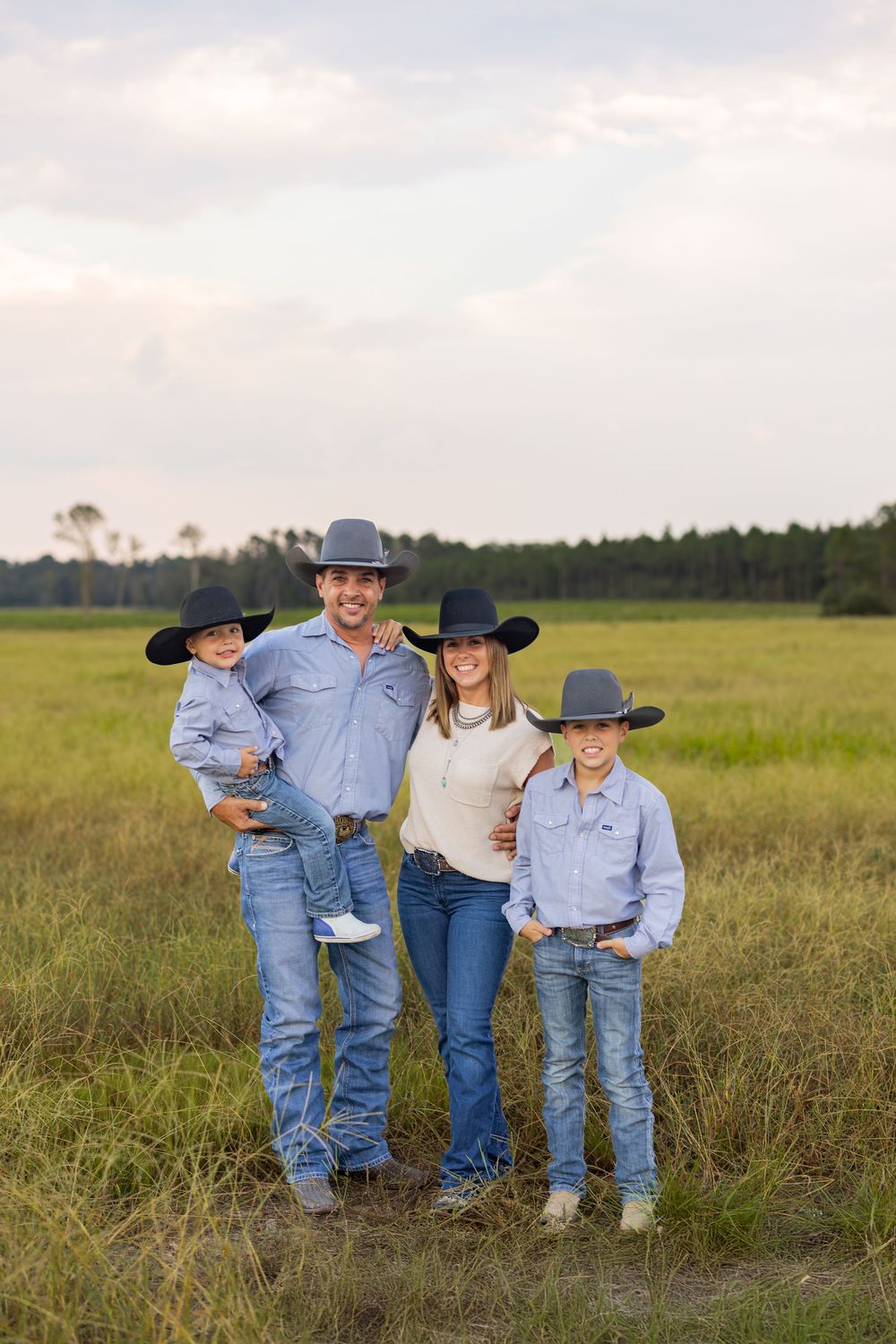 Family dressed in western wear standing together in a grassy field at sunset.