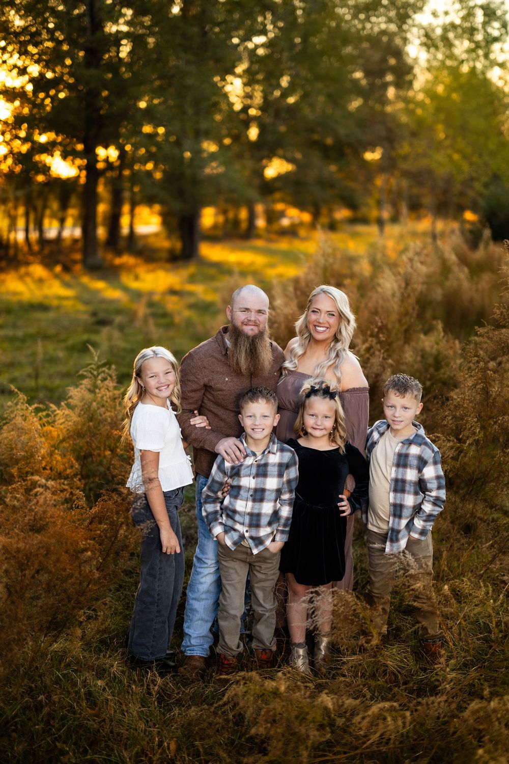 Family portrait in autumn field with golden sunlight filtering through trees.