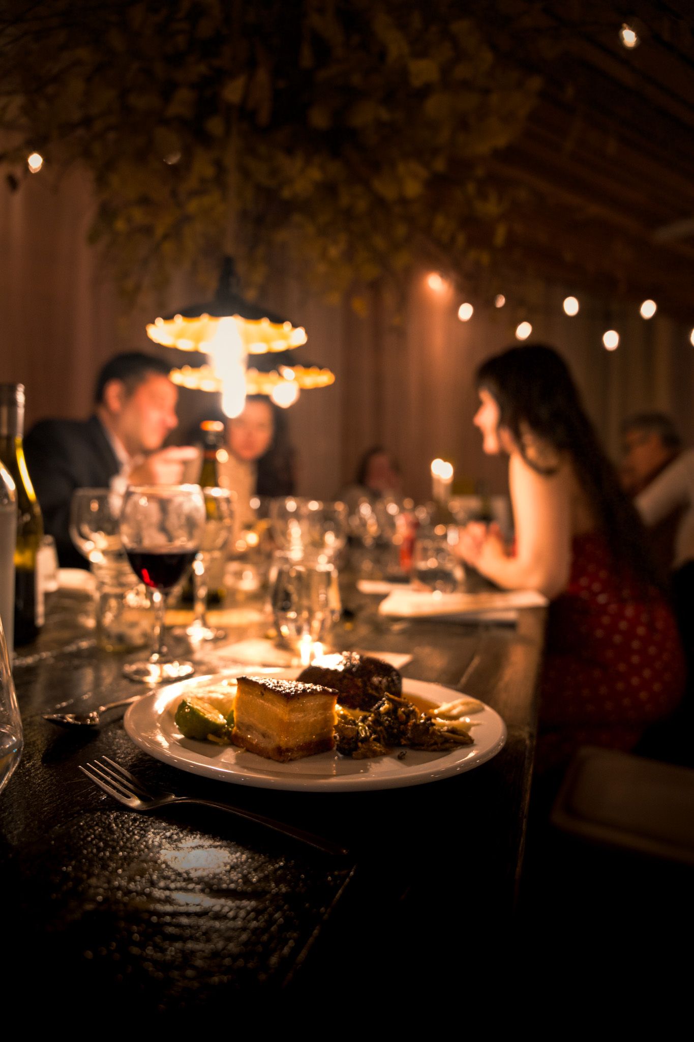 Elegant dinner setting with dessert plate in foreground and romantic ambient lighting.