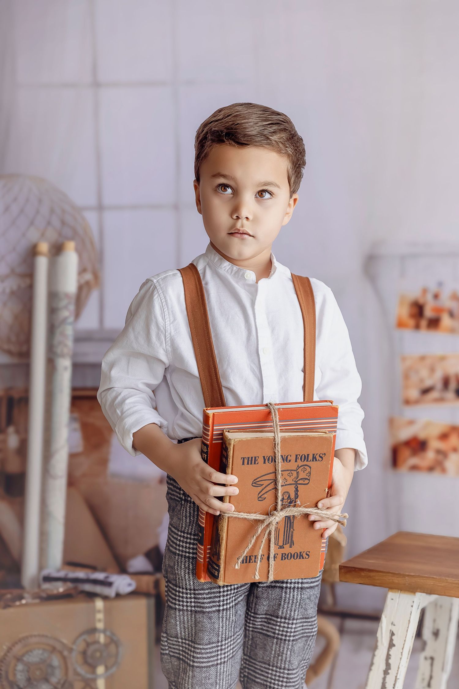 Nino de 5 anos aguanta libros para unas Fotografias vintage tiene un atuendo de tirantes.