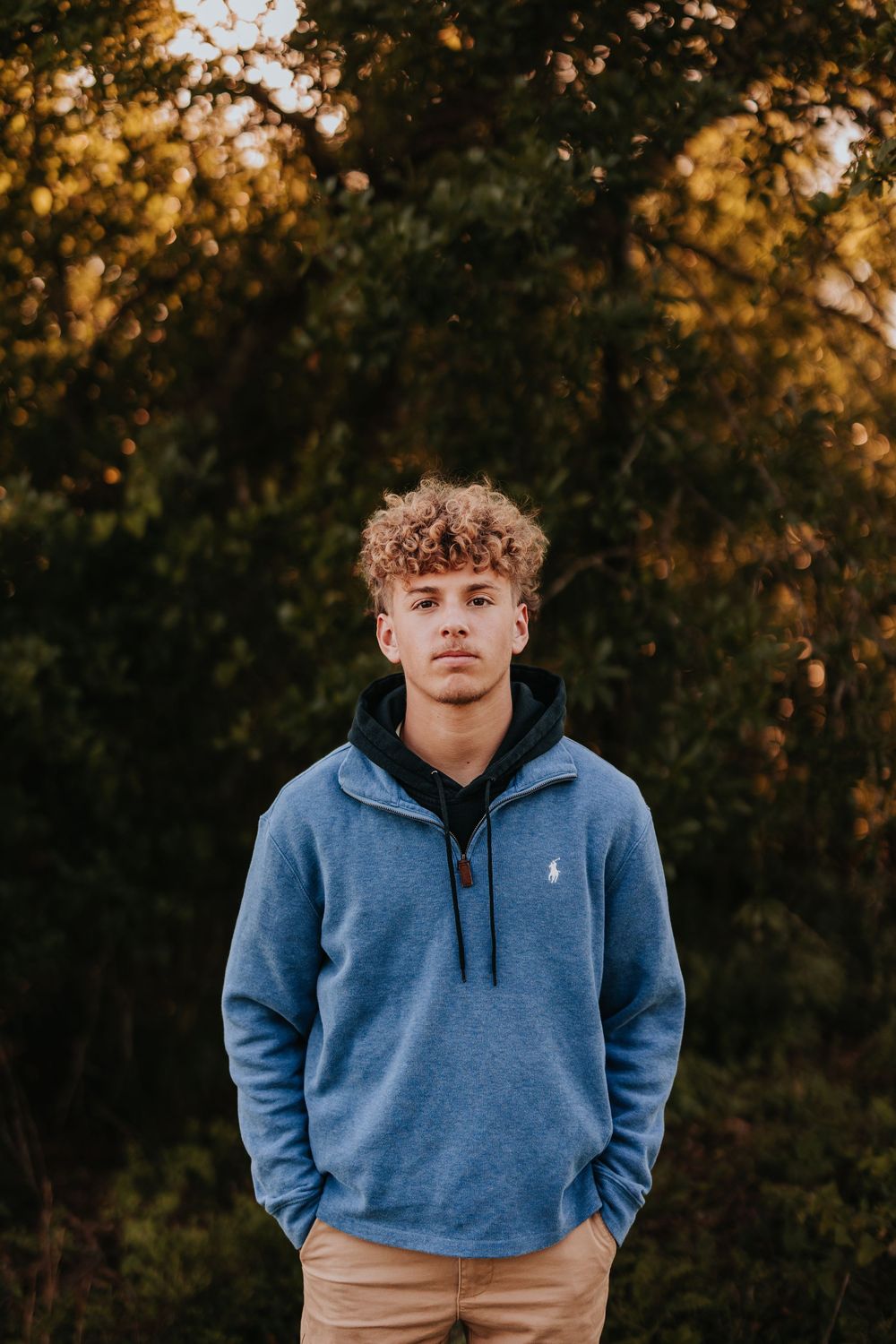 Person in blue hoodie standing against autumn trees at sunset.