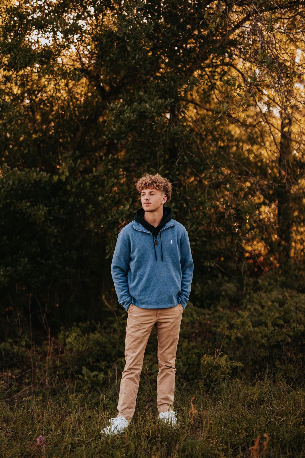 Casual portrait of someone in blue sweatshirt and khakis against fall foliage.