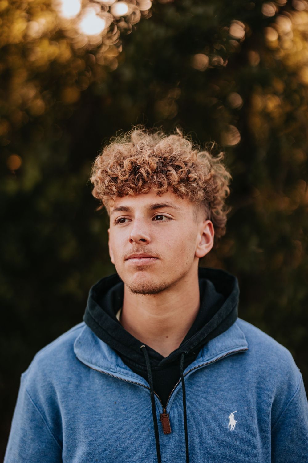 A young person in a blue Ralph Lauren hoodie poses against a warm autumn background with bokeh lighting effects.