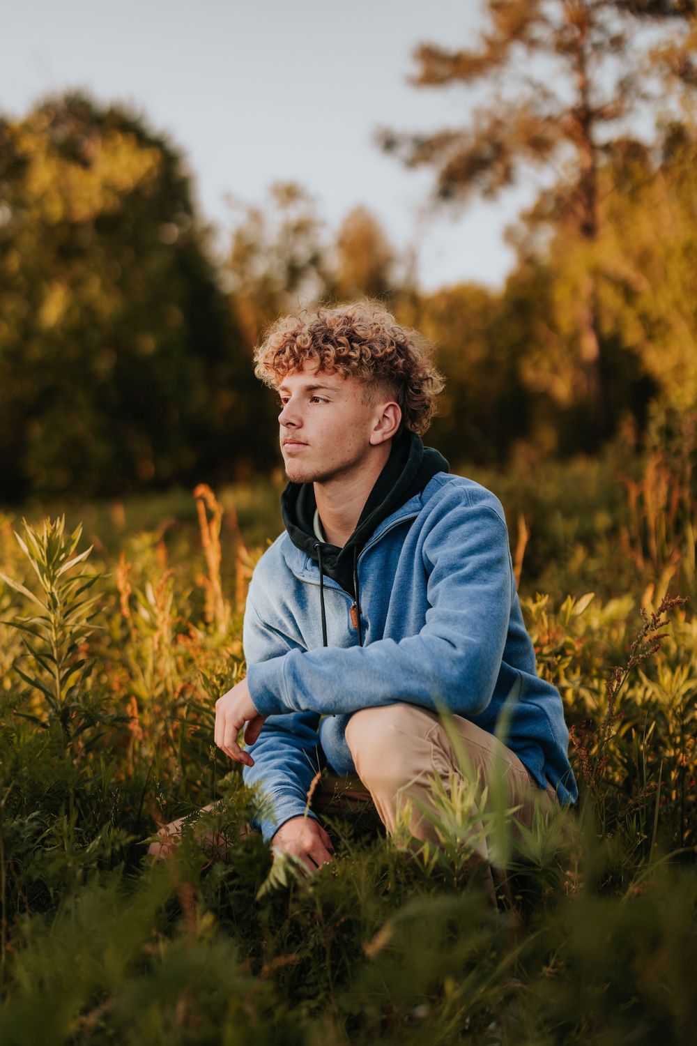 Person relaxes in tall grass during golden hour wearing casual blue hoodie.