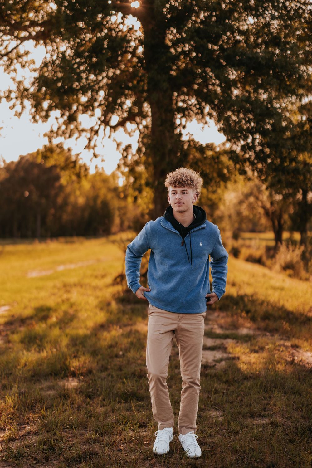 Person in blue hoodie and khaki pants walks on hillside path during sunset.