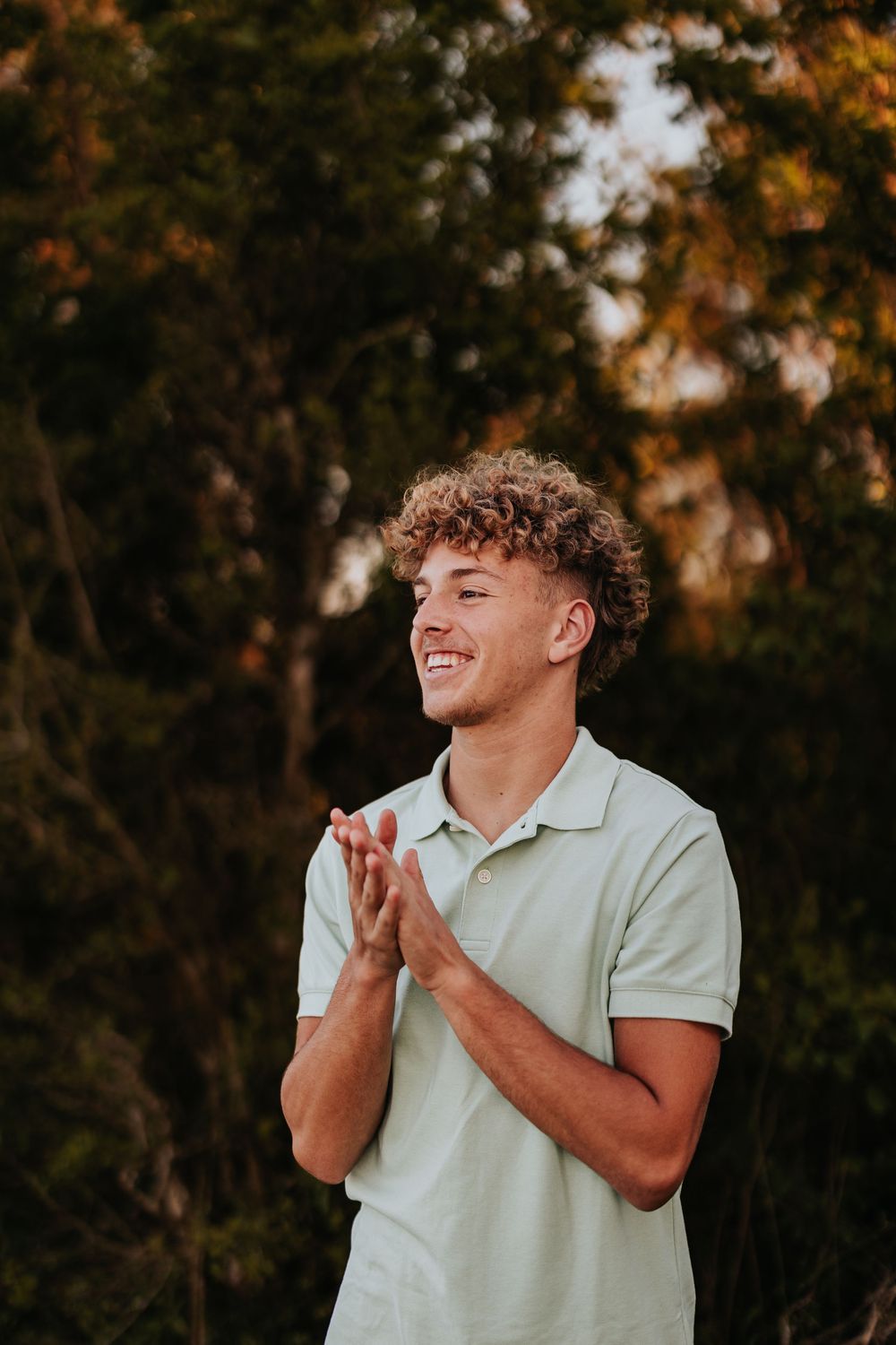Person in white polo shirt makes excited gesture outdoors at sunset.