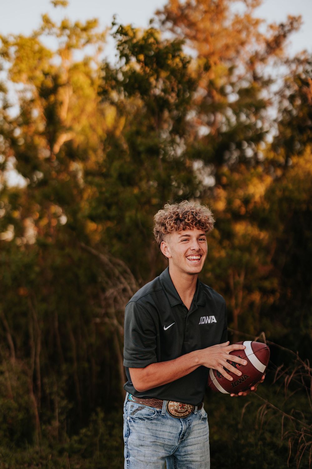 Person in black Nike shirt plays with football during golden hour photoshoot.