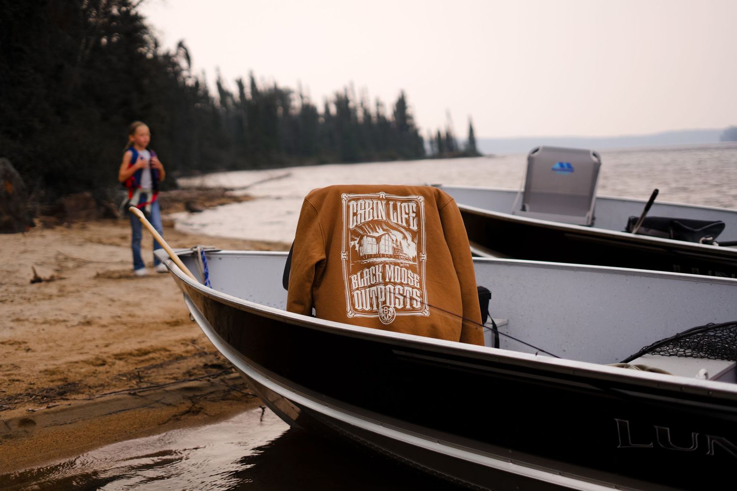 Wooden canoe with Boundary Waters logo gliding across a serene lake surrounded by pine forests.