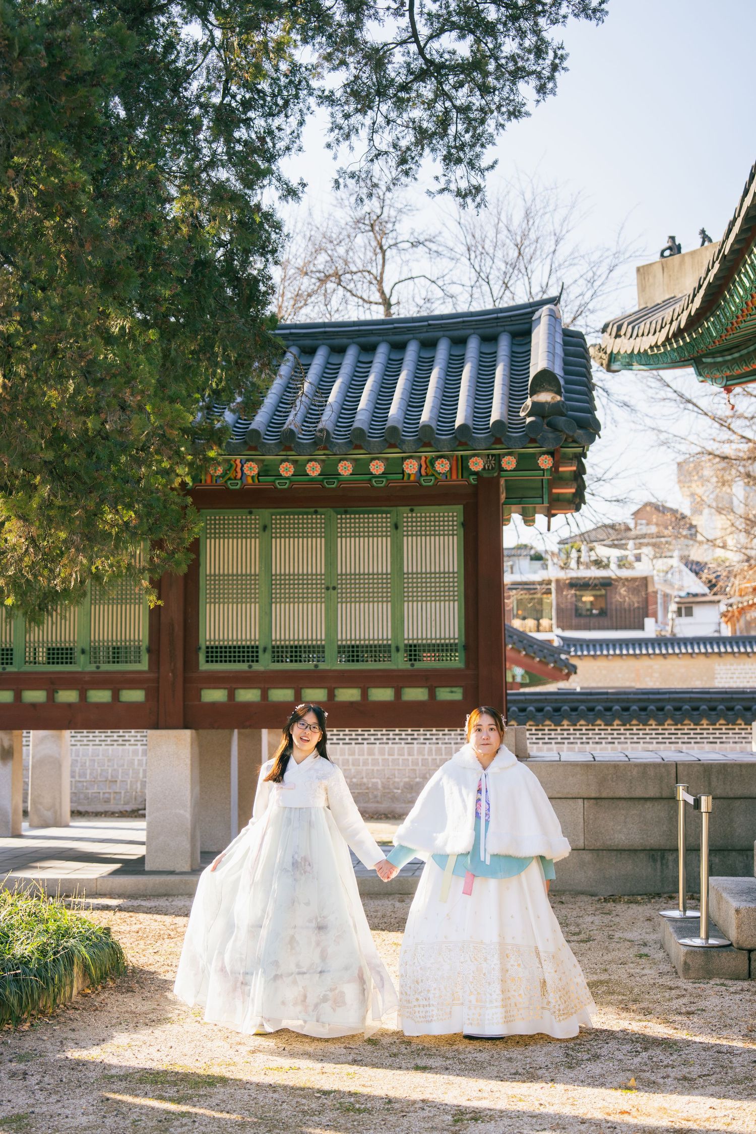 Traditional Korean hanbok dresses displayed in a scenic courtyard with traditional architecture and autumn foliage.