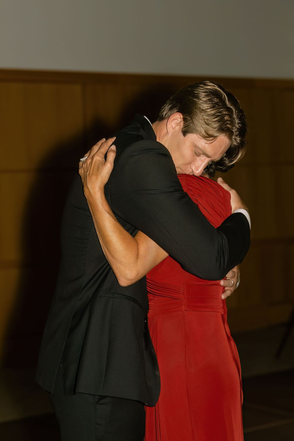 A couple shares a close dance moment in formal evening attire under dim lighting.