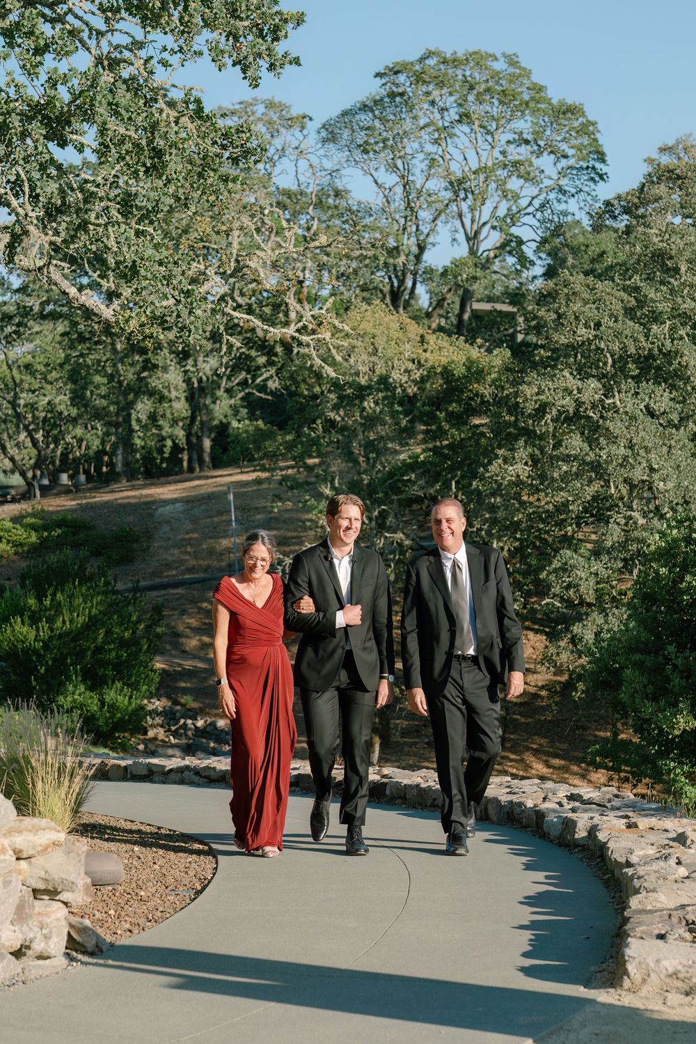 Wedding party walking along a curved pathway surrounded by landscaped gardens.