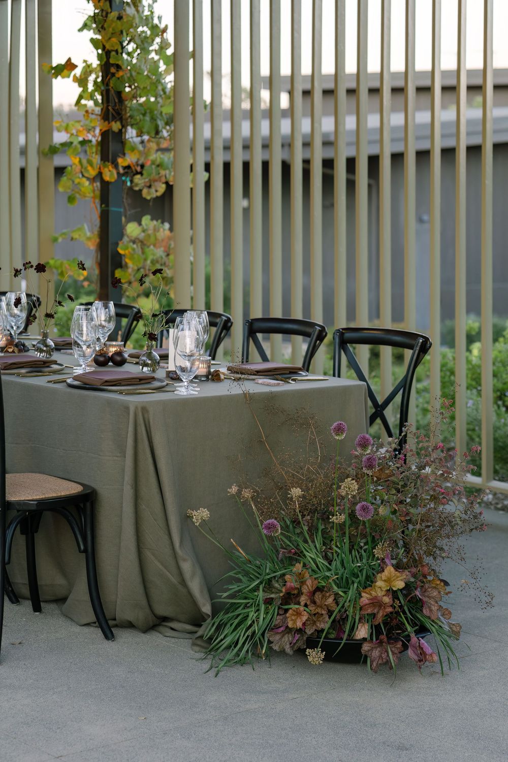 Close-up of elegant table settings with natural floral arrangements and grey linens against vertical slats.