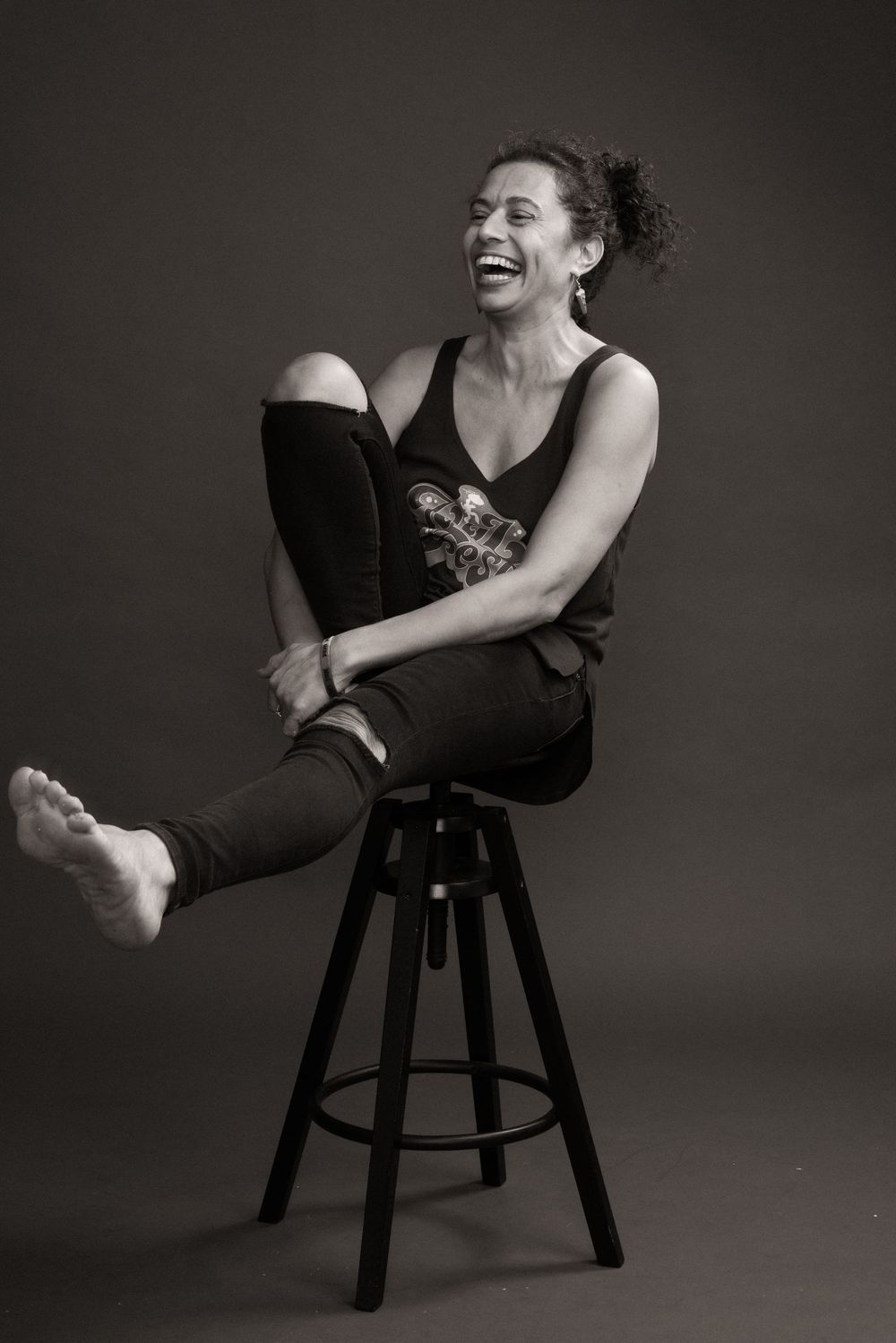 Black and white portrait series showing joyful laughter and movement while seated on a dark stool against gray backdrop.