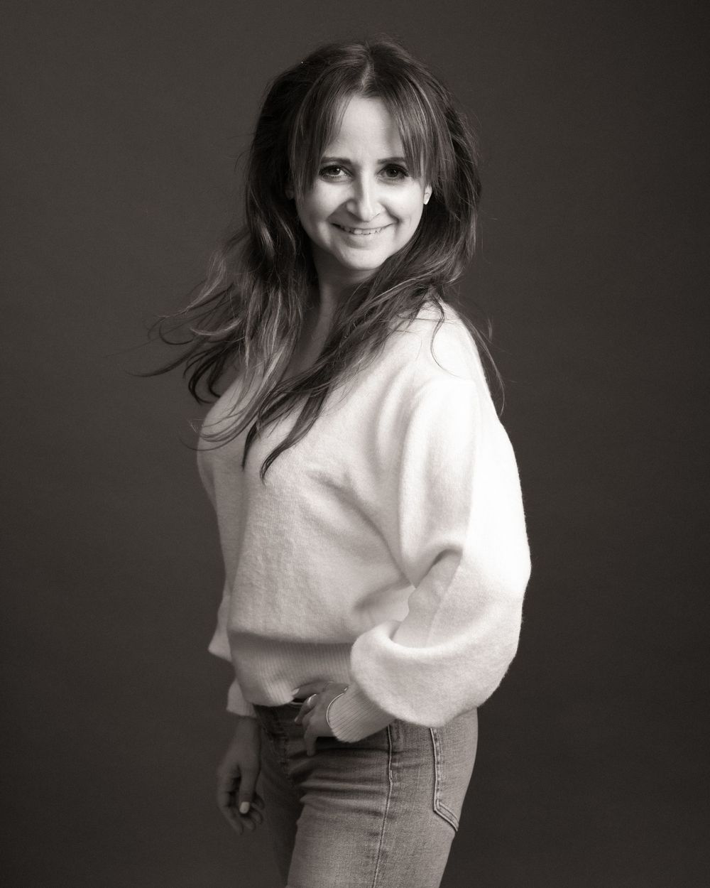 A series of black and white portraits showing someone posing in a white sweater and dark skirt against a dark backdrop.
