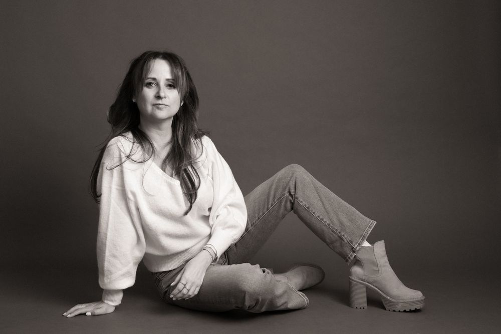 Black and white portrait of a woman in casual attire sitting on floor wearing white sweater and jeans.