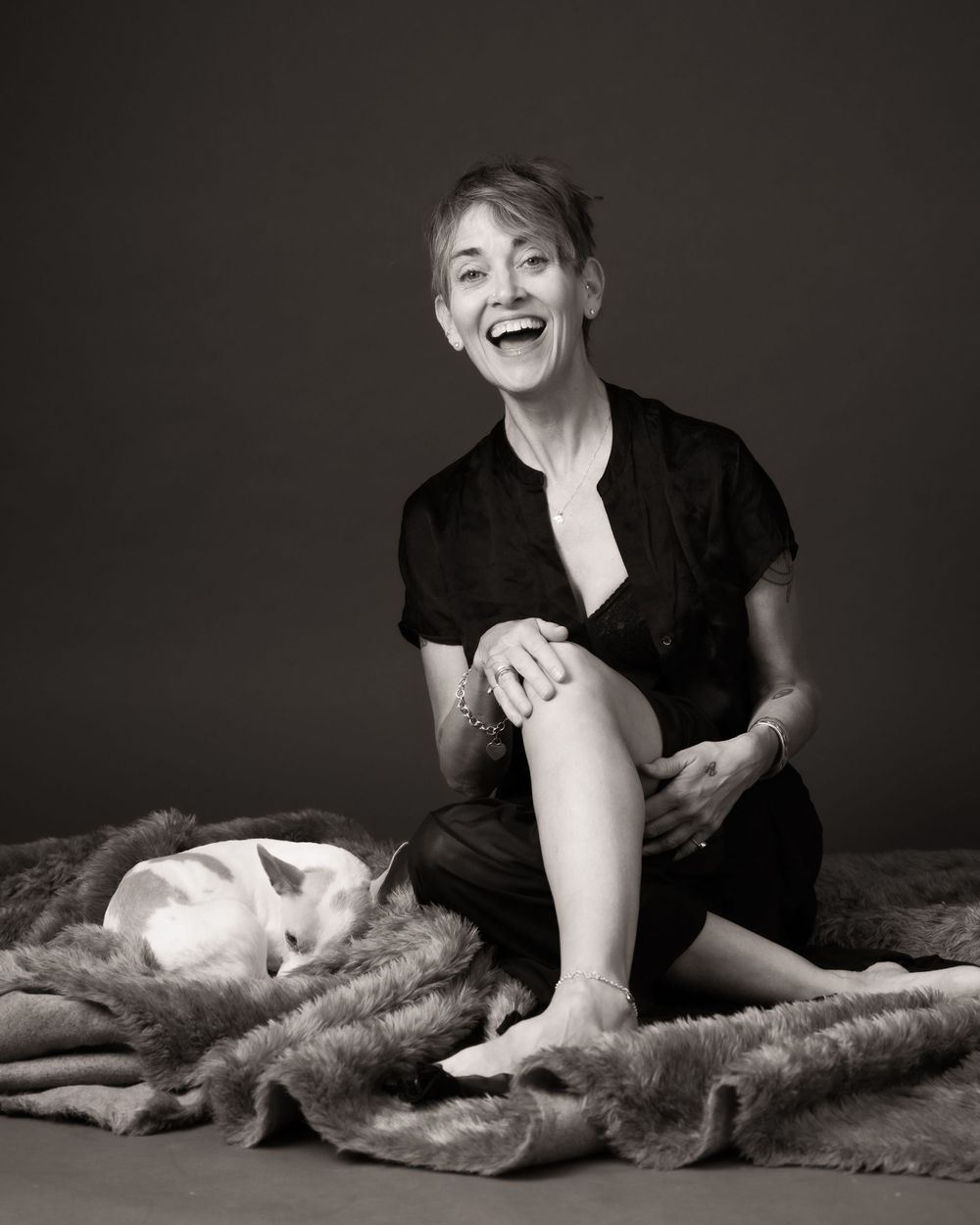 A series of black and white artistic portraits showing someone in black attire reclining on a furry rug with expressive poses.