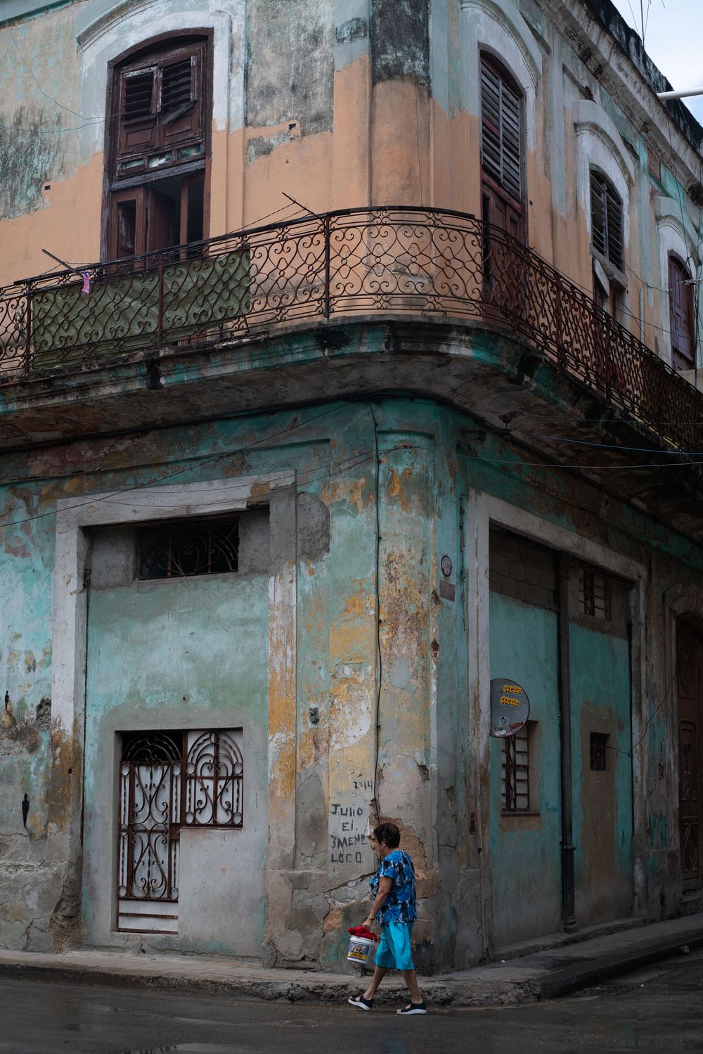 Weathered turquoise building corner with peeling paint and ornate balconies in old Havana.