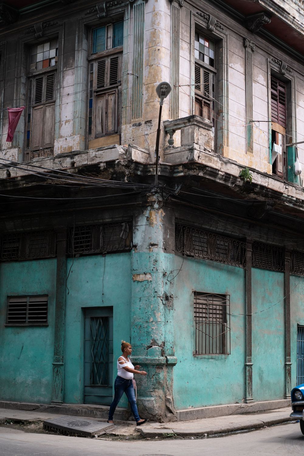 Decaying turquoise corner building with wrought iron balconies in urban setting.