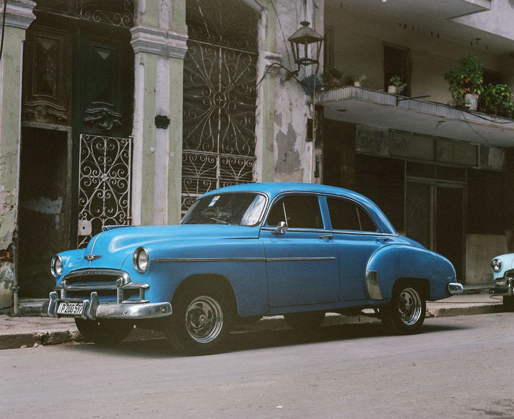Row of vintage blue cars parked along a street with historic buildings.