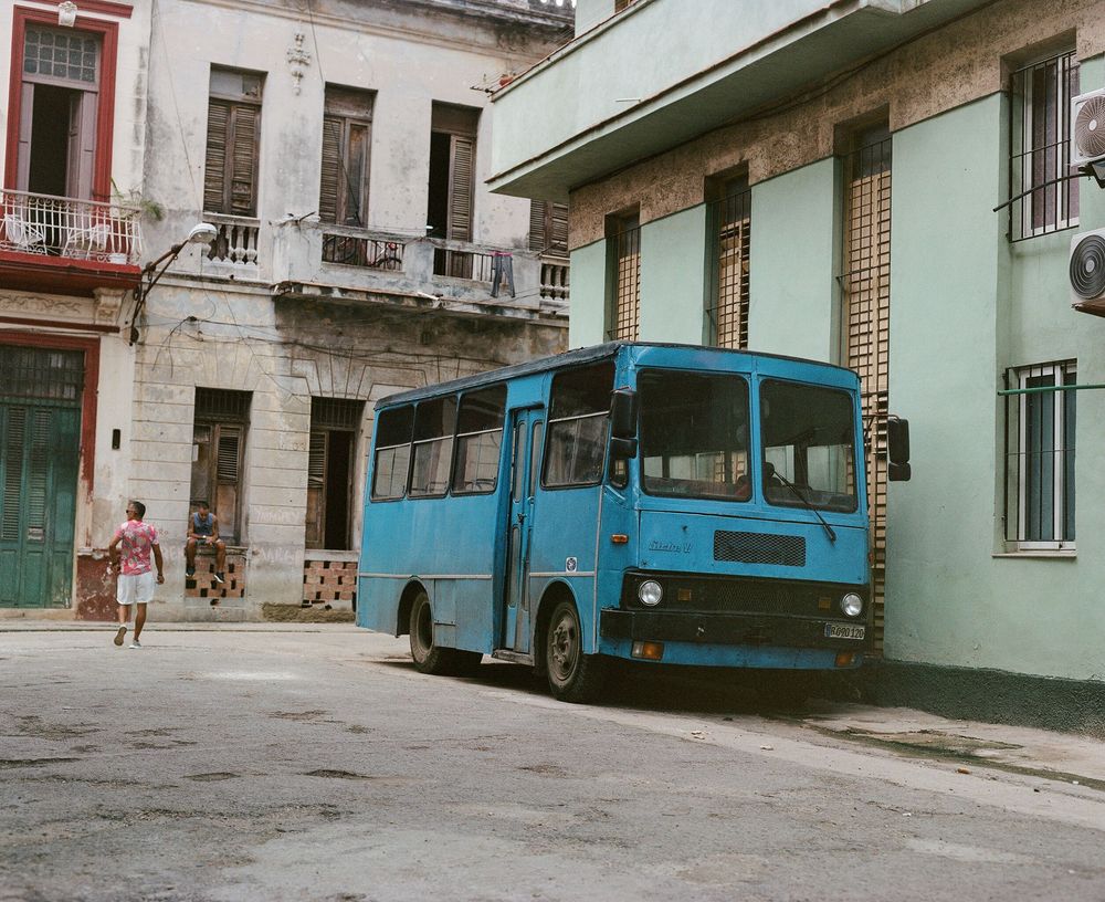 Vintage blue buses parked along a street with old buildings in Cuba.