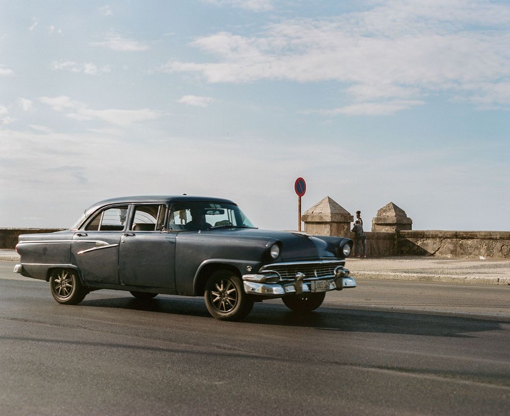 Classic vintage cars lined up on a desert road against a cloudy sky.