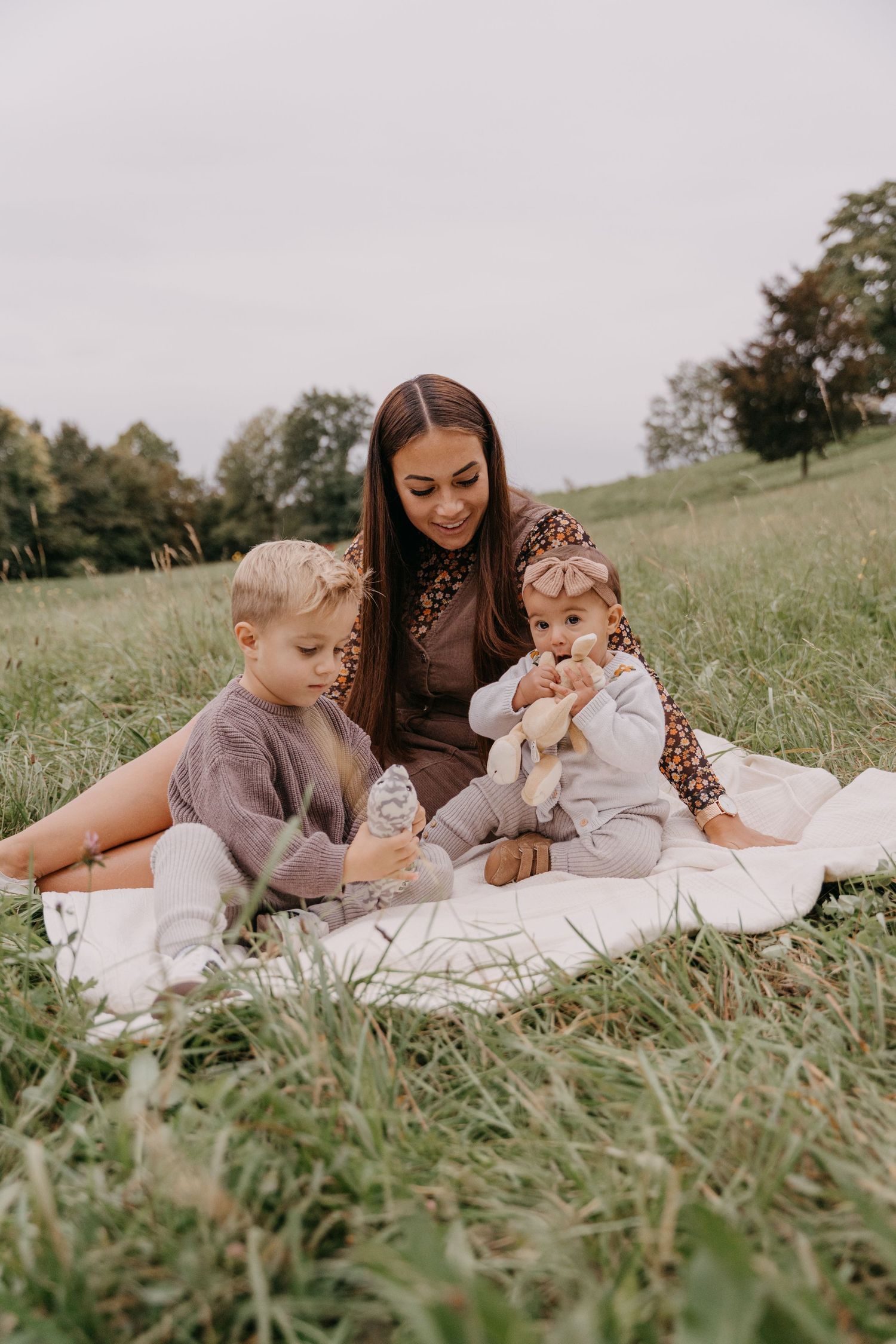 Family sitting together on white blanket in grassy field during outdoor photo session.