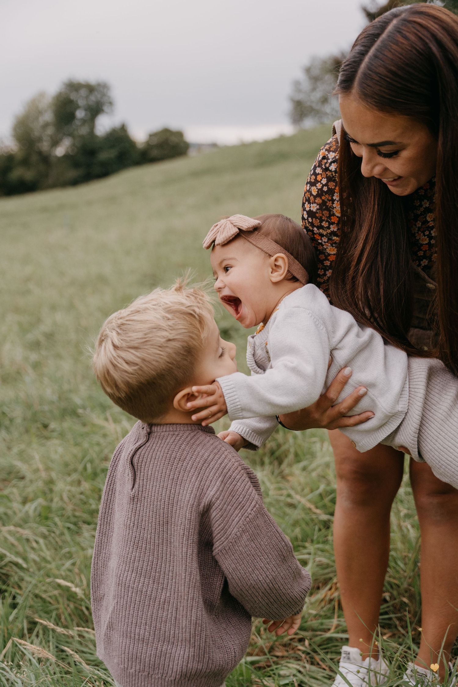 A tender moment captured in a grassy field shows a parent and child in neutral knit sweaters playing together.