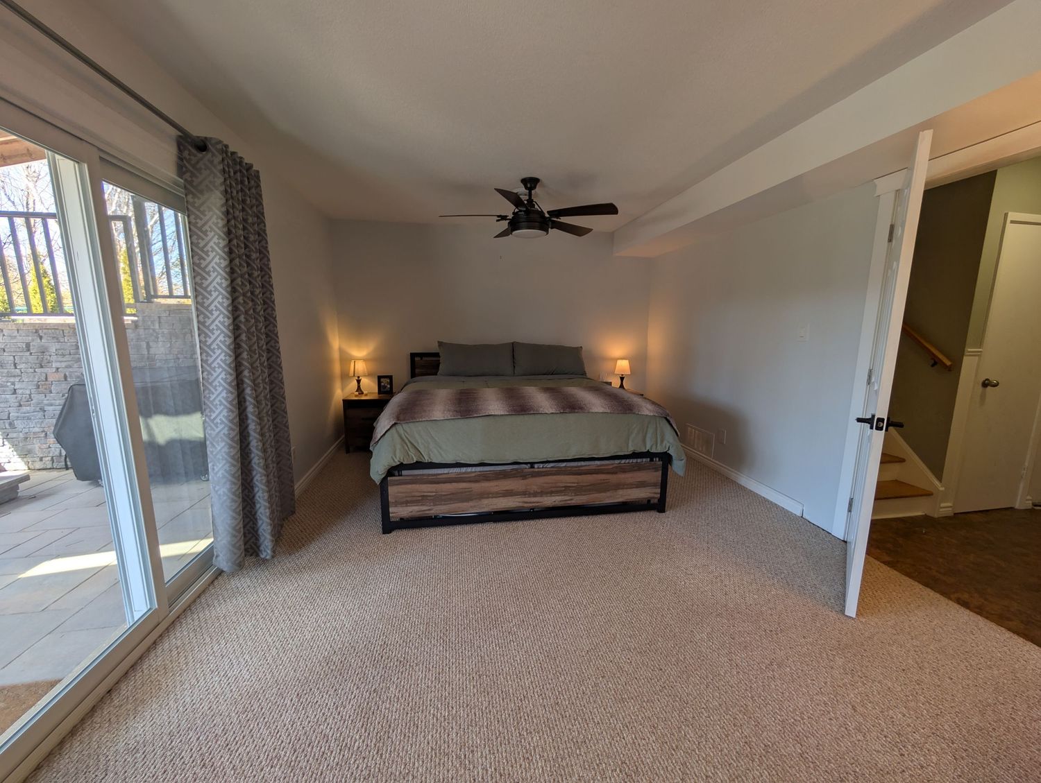 Beige carpeted bedroom with natural light features ceiling fan, large windows, and neutral walls.