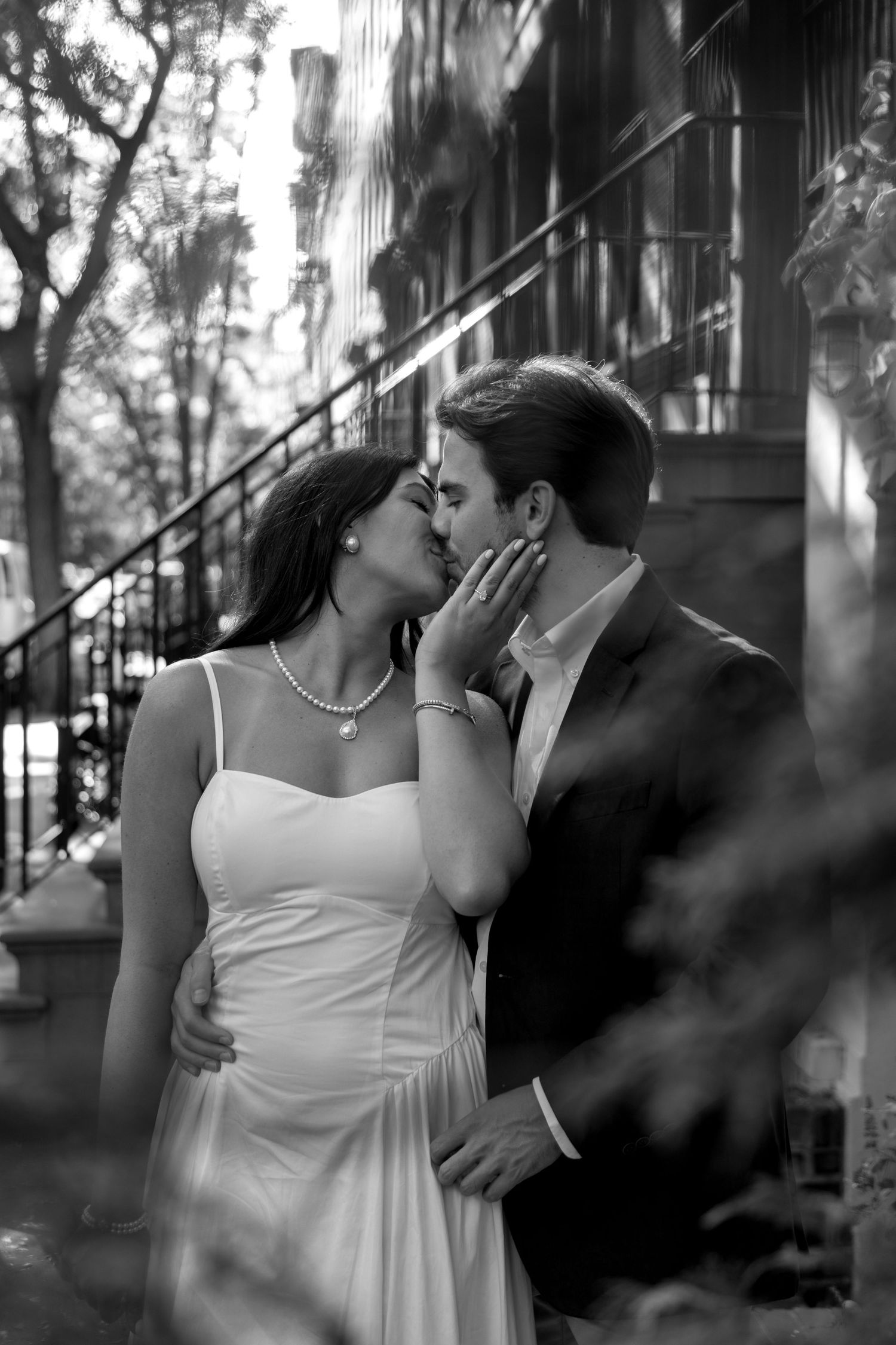 A romantic black and white photo of a couple sharing an intimate moment on a brownstone staircase.