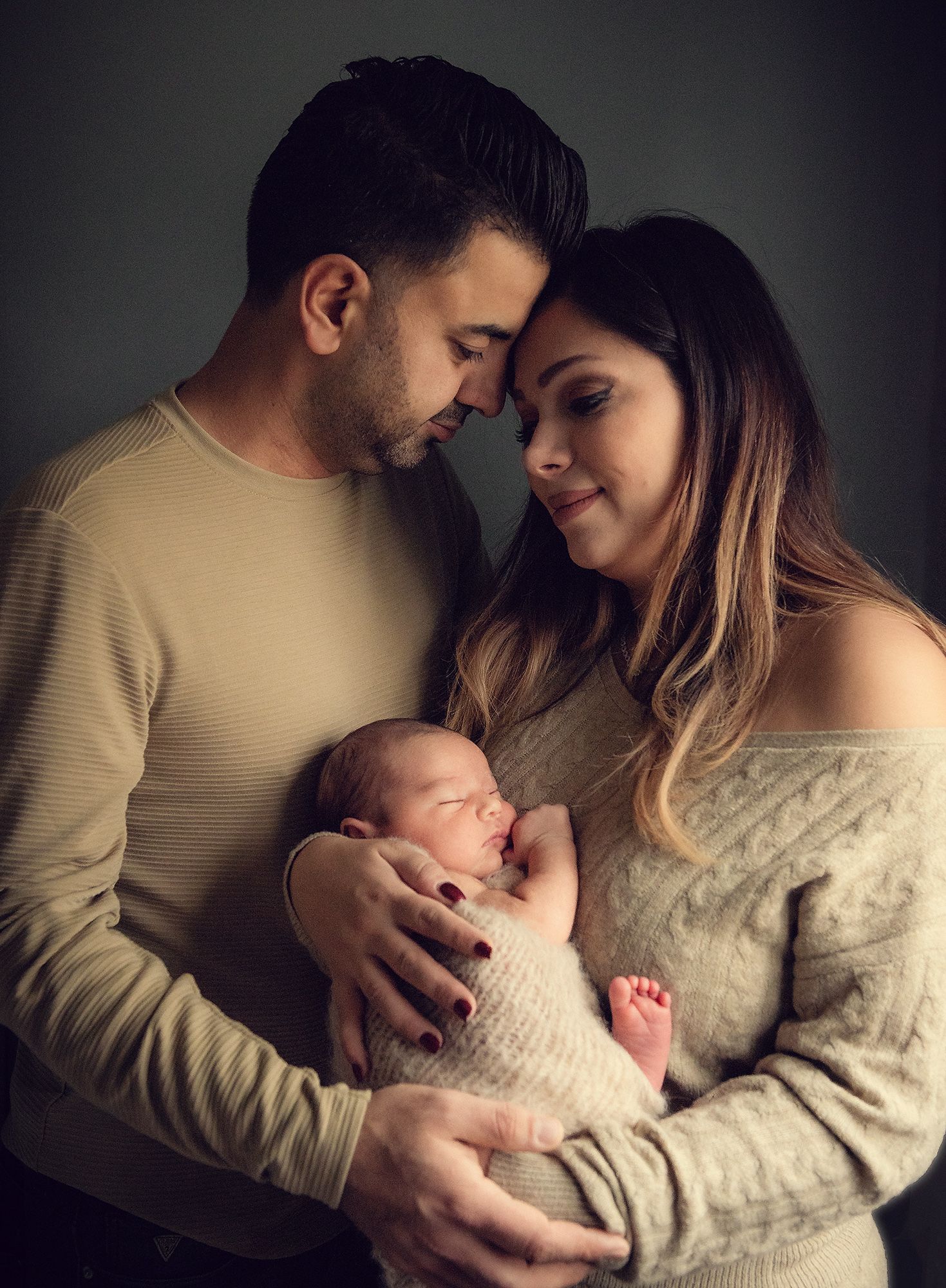 A couple in cream and white sweaters cradle their newborn baby in a series of intimate black and white portraits.