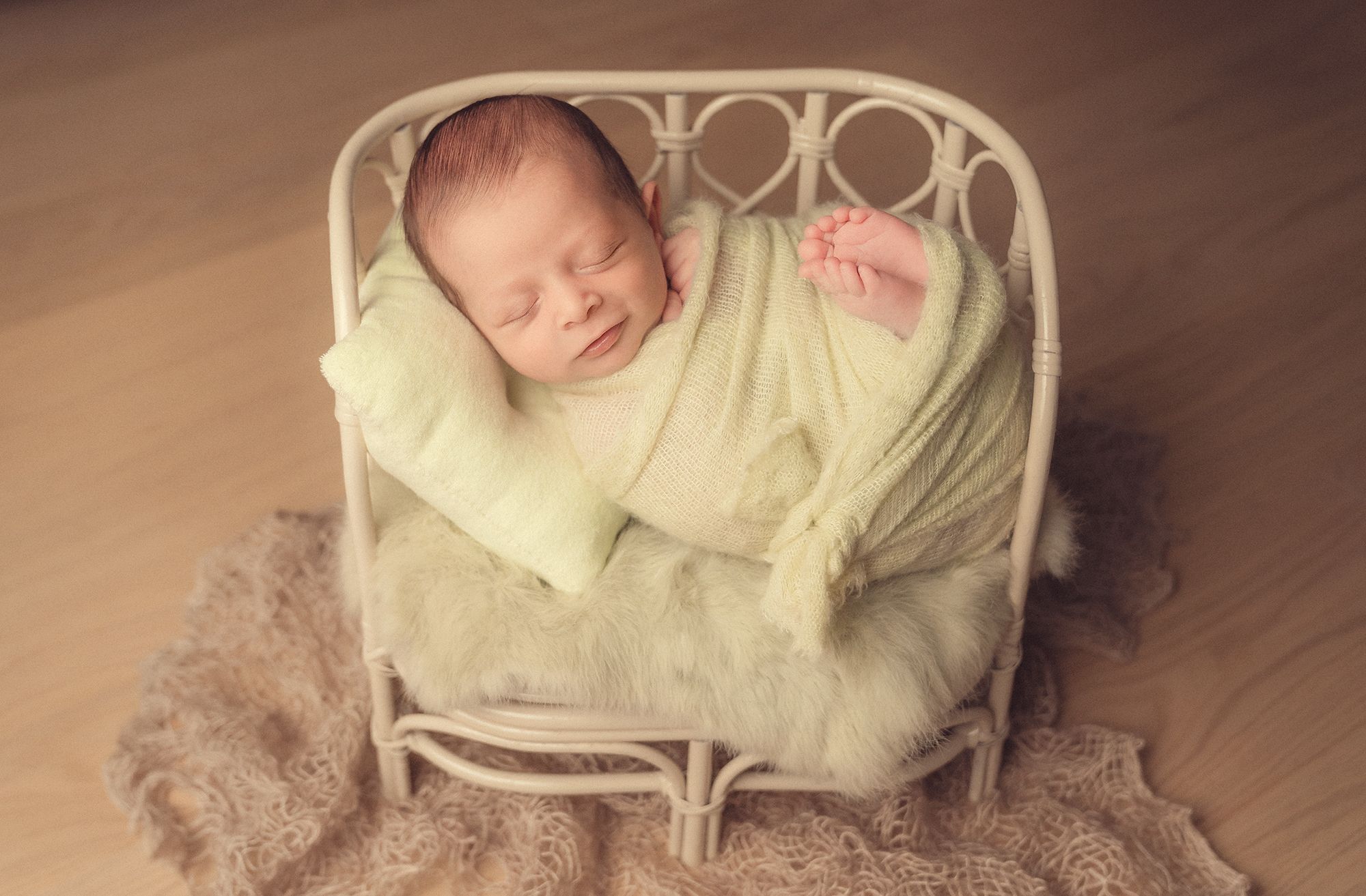 A sleeping baby wrapped in a soft yellow blanket lies peacefully on a beige carpet.