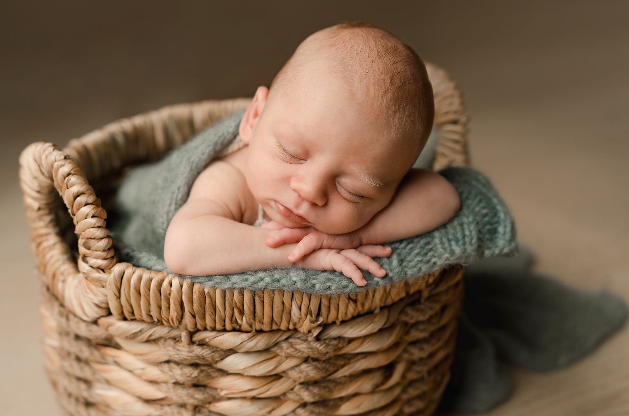 A sleeping newborn baby wrapped in soft fabric lies peacefully in a woven wicker basket.