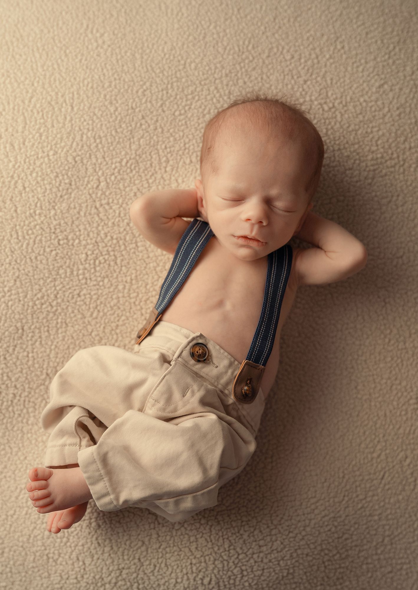 A sleeping baby wearing tan overalls lies peacefully on a beige carpet in a series of gentle poses.
