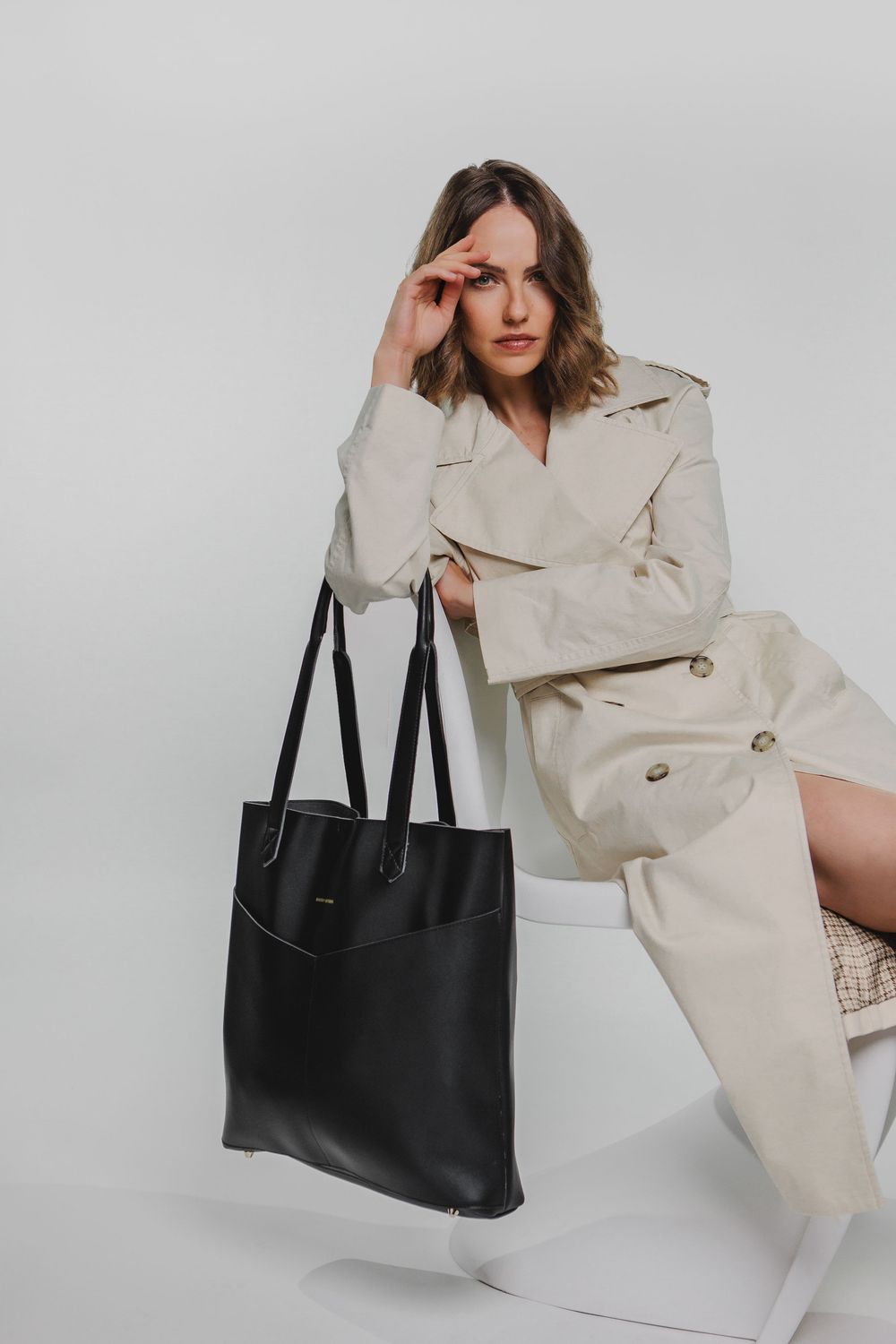 Lifestyle product photography series showing a black leather tote bag with a cream trench coat against white background.