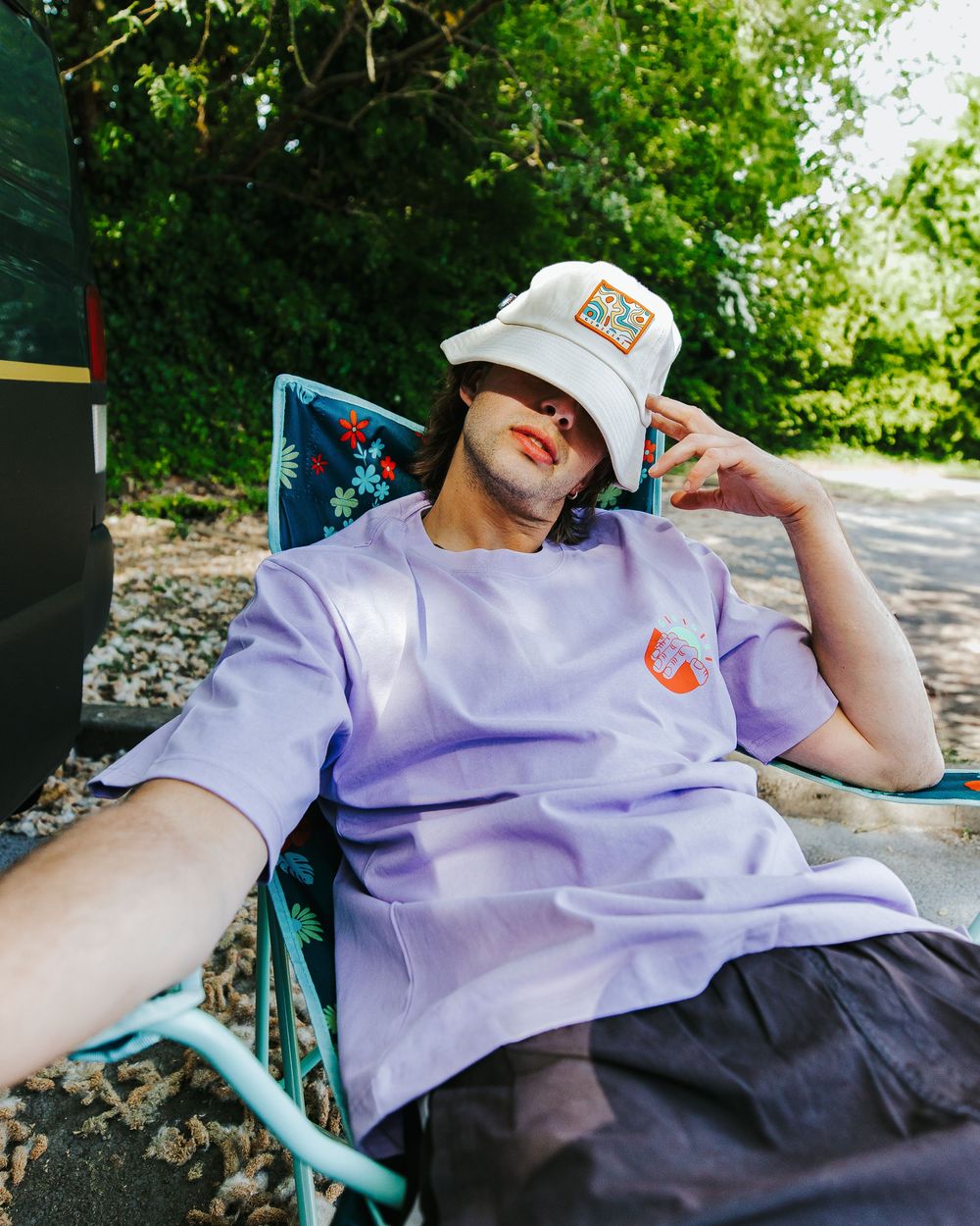 Person in a purple shirt and baseball cap relaxing in an outdoor setting.