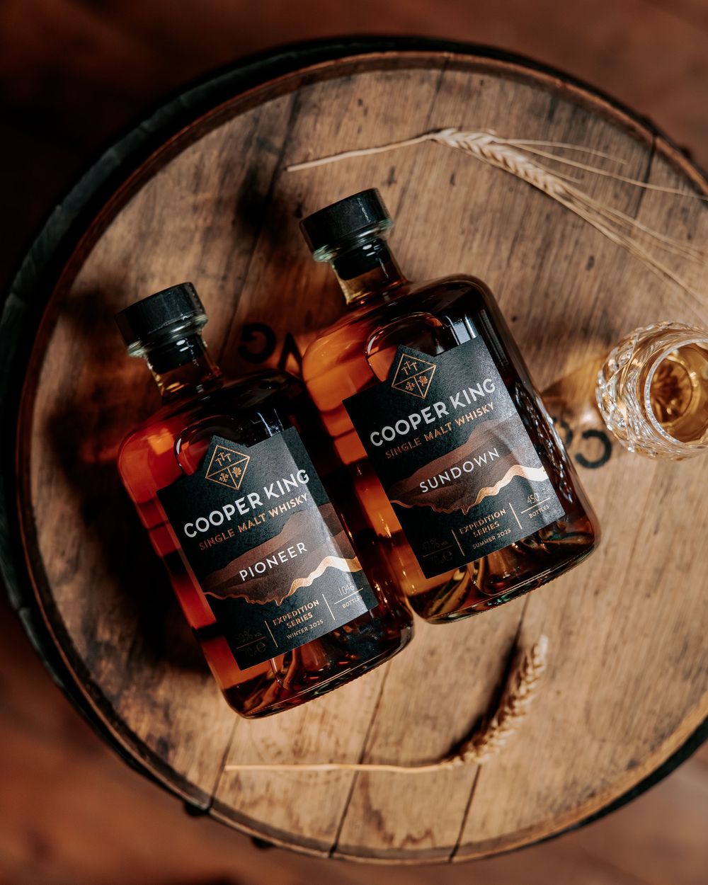Multiple bottles of Cooper King whiskey displayed on a rustic wooden barrel in moody lighting.