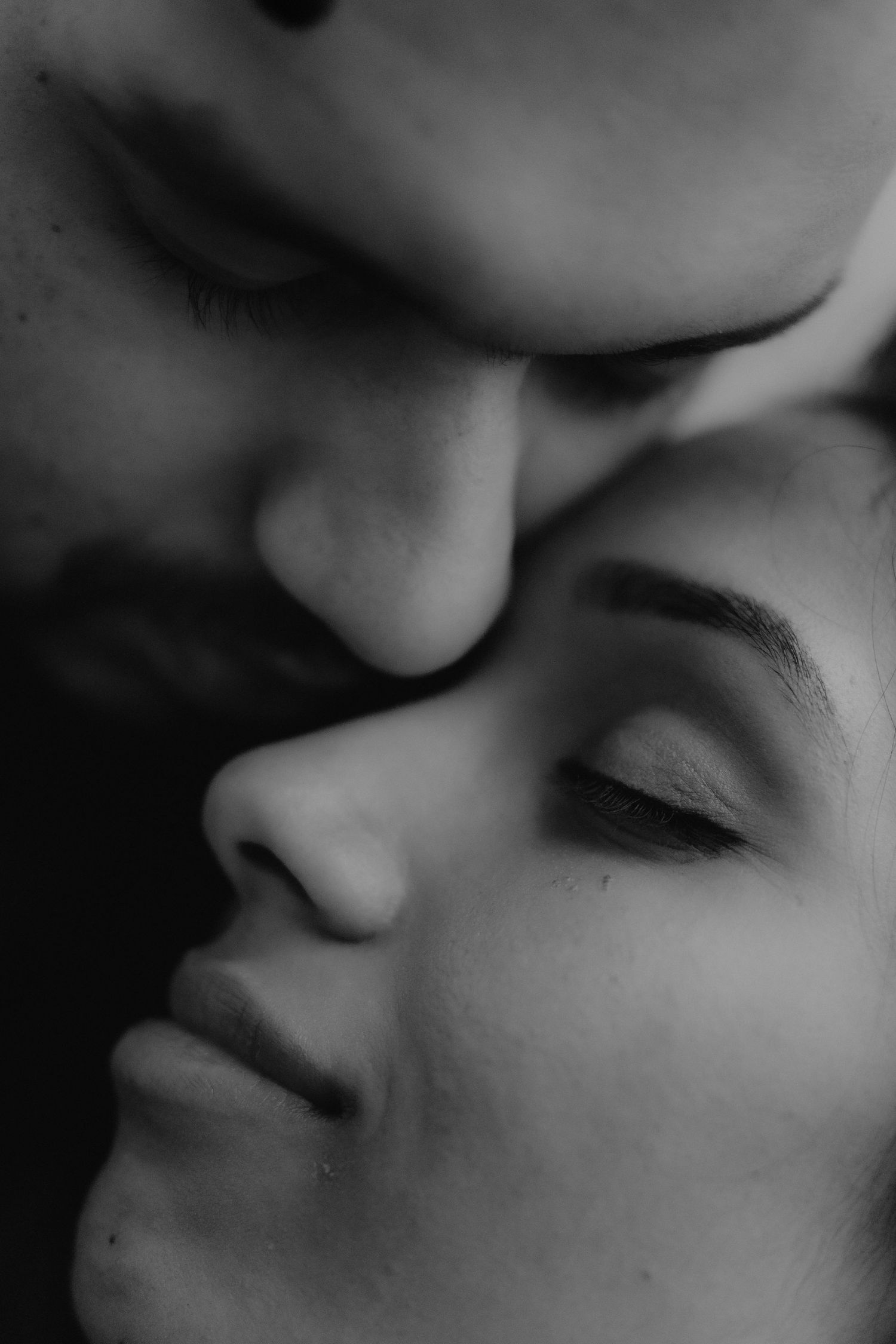 Black and white close-up of two people sharing an intimate moment, faces nearly touching with eyes closed.